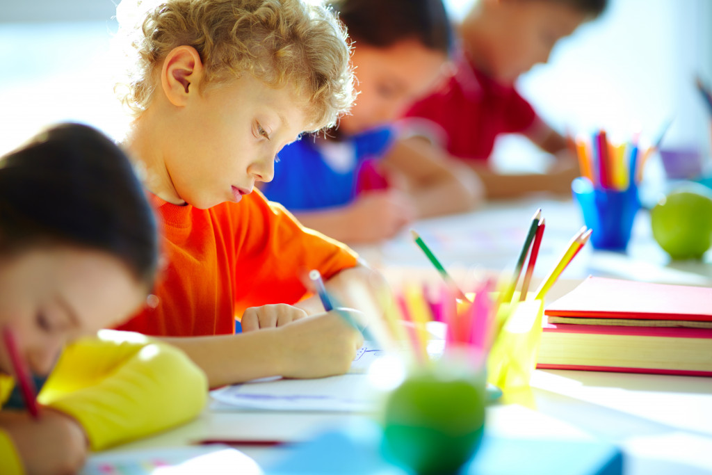 Portrait of cute schoolboy drawing at workplace among his classmates